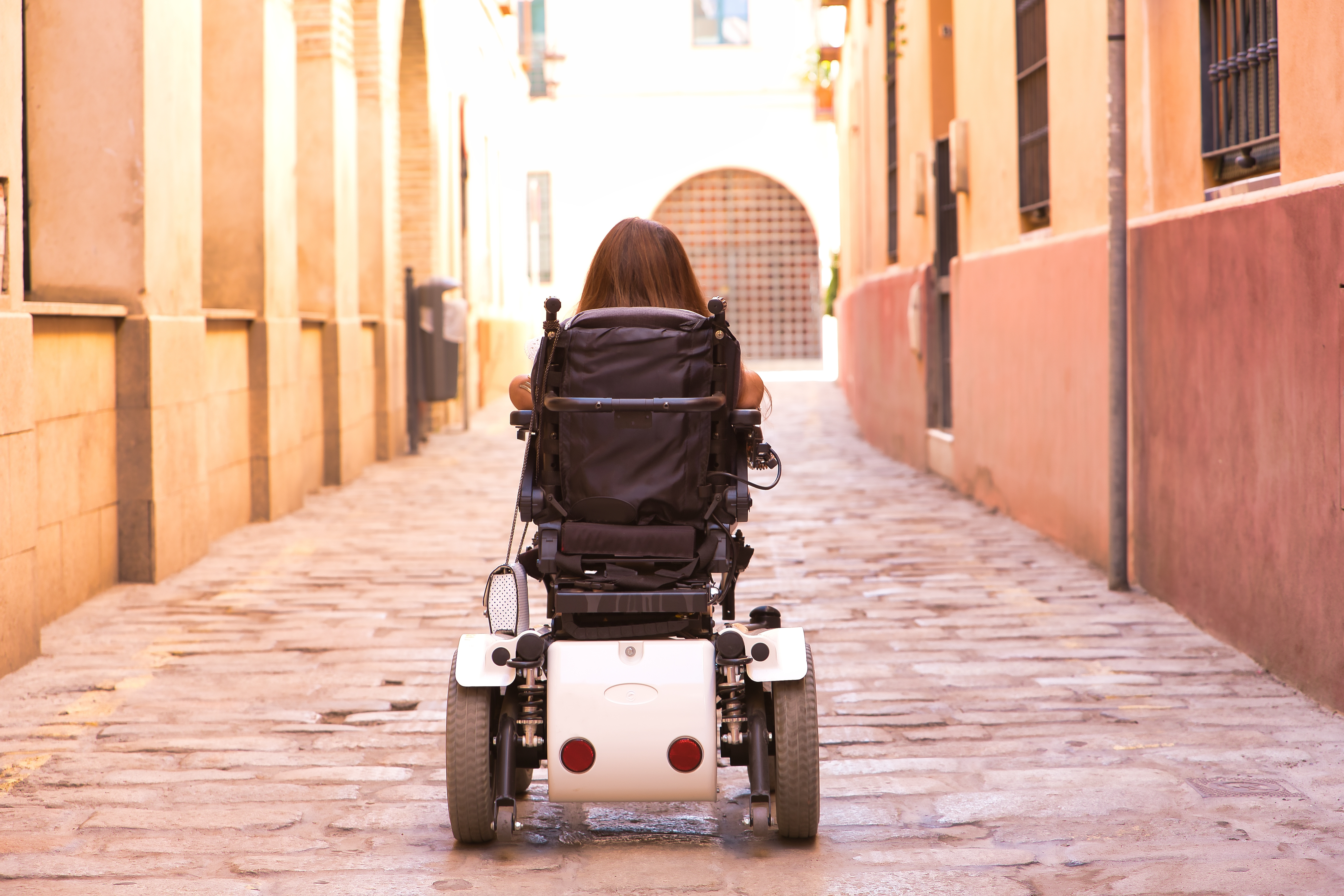 Woman navigating a power wheelchair down a cobblestone street. 