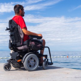 Man on wheelchair looking at ocean on summer vacations.