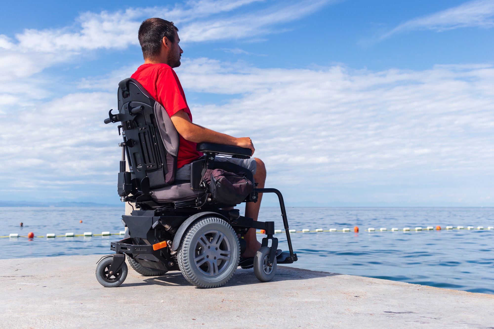 Man on wheelchair looking at ocean on summer vacation.