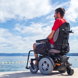 Man sitting in a power wheelchair looking out over the water. 