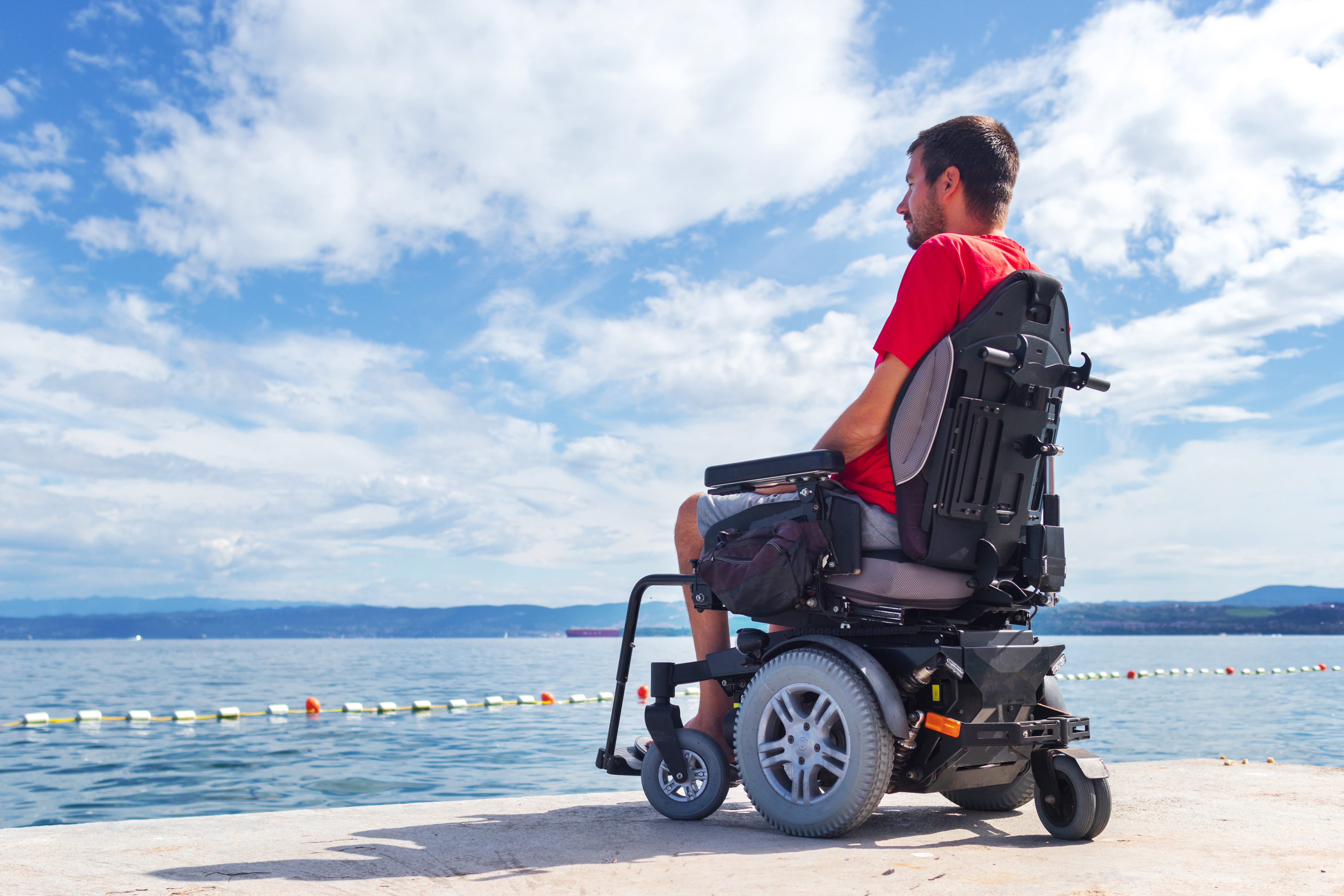 Man sitting in a power wheelchair looking out over the water. 