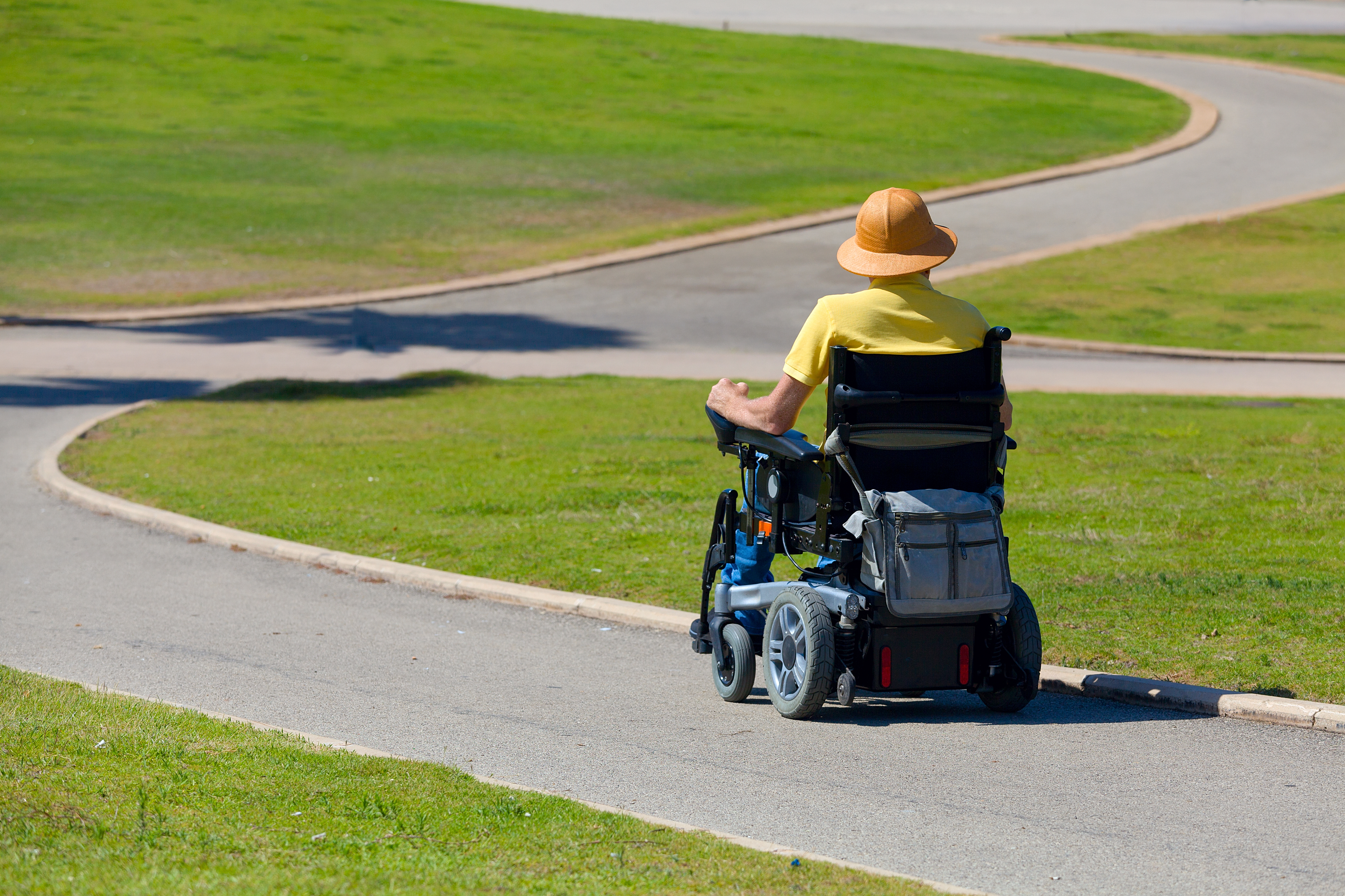 Man in wheelchair strolling down an inclined sidewalk