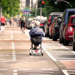 Older woman driving down the street in an electric wheelchair. 