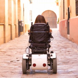 Woman navigating a power wheelchair down a cobblestone street. 
